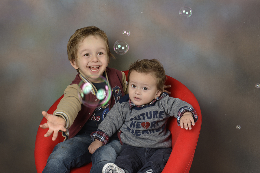 zwei kleine Buben sitzen auf einem roten Stuhl und fangen Bubbles, Seifenblasen